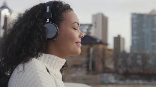 Woman with headphones and phone smiling in urban setting