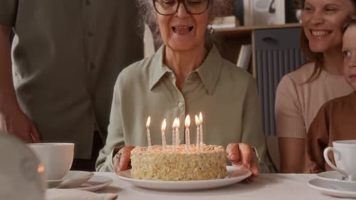 Woman blowing out birthday candles surrounded by family