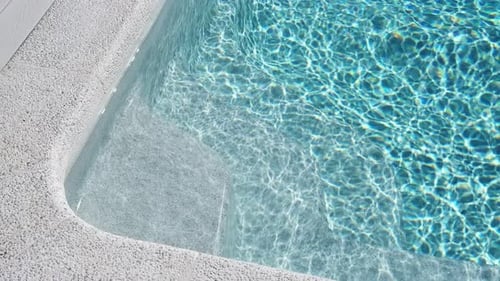 Leichte Betonstufen in einem Swimmingpool mit sauberem blauem Wasser und Sonnenlichtreflexen. Oberflächentext