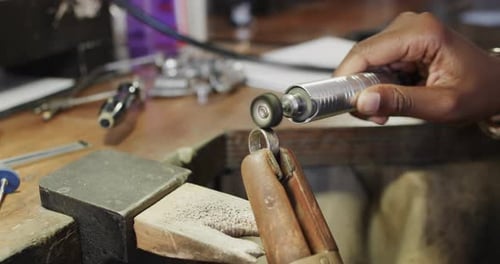 Biracial female worker shaping ring using handcraft tools in workshop in slow motion