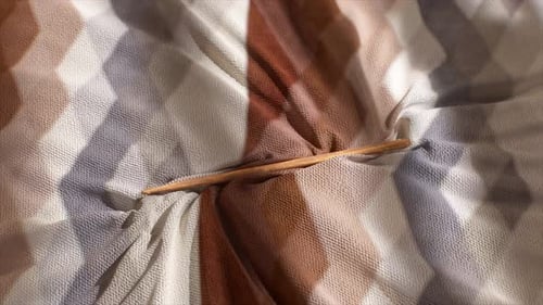 Nahaufnahme eines bunt strukturierten Stoffes mit geometrischen Mustern, in den ein Holzwerkzeug eingeführt wurde
