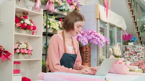 Young Caucasian florist owner works with laptop in colorful flower shop store.
