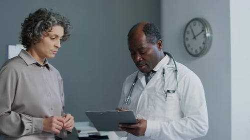 Doctor Discussing Clipboard with Woman in Office
