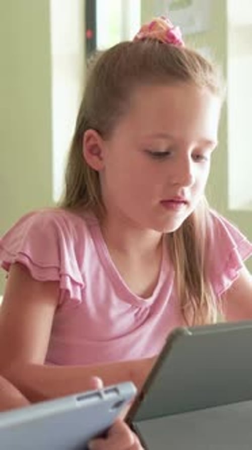 Vertical video: Looking down, girl in pink shirt studying on tablet at school, neighbor's tablet