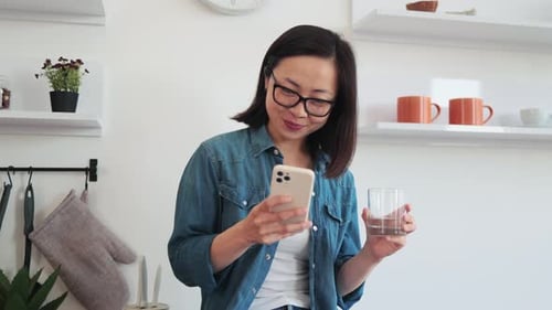 Smiling Woman Using Phone in Bright Kitchen