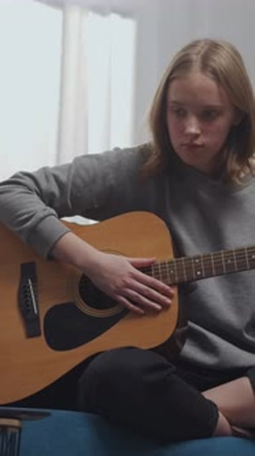 Teen Girl Practicing Acoustic Guitar at Home During Online Music Lesson Focusing on Chords and
