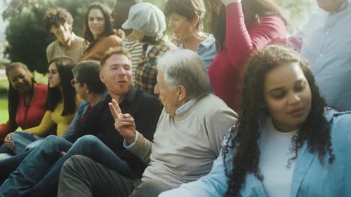 Happy multigenerational people with different ethnicity having fun sitting on grass in a public park