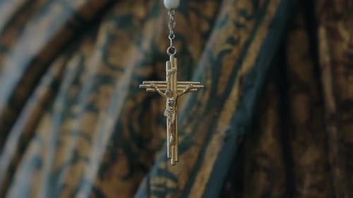 Golden crucifix pendant hanging against ornate fabric backdrop