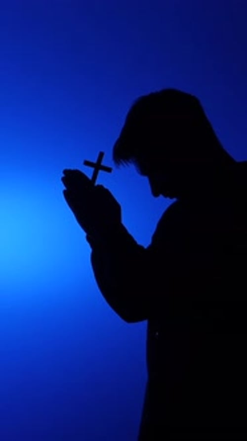 Silhouette of person holding cross on blue background