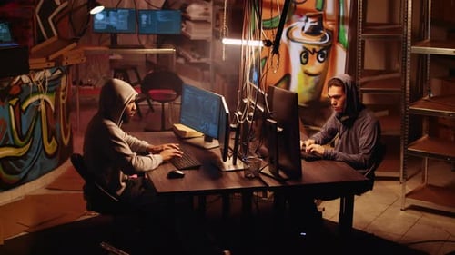Two Young Adults Hacking Computers in Graffiti Room