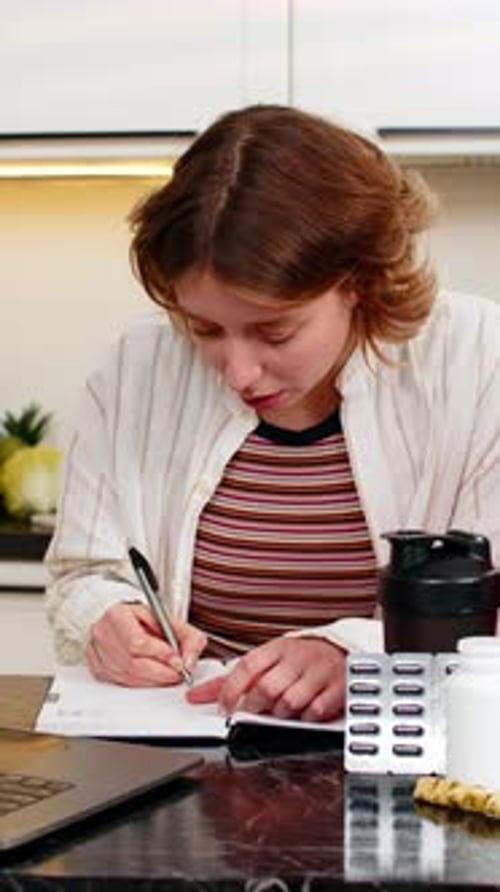 Woman with Supplements Taking Notes at Kitchen Table