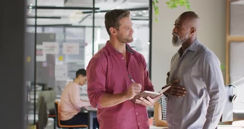 Happy diverse business people holding notebook and discussing work at office