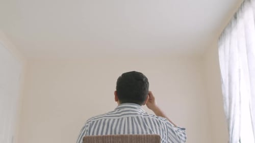 A Back View Of A Guy Sitting While Looking Around The Room And Scratching His Head