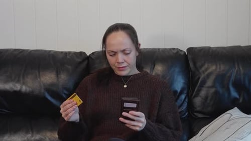 Woman with Card Looking at Phone Indoors on Couch