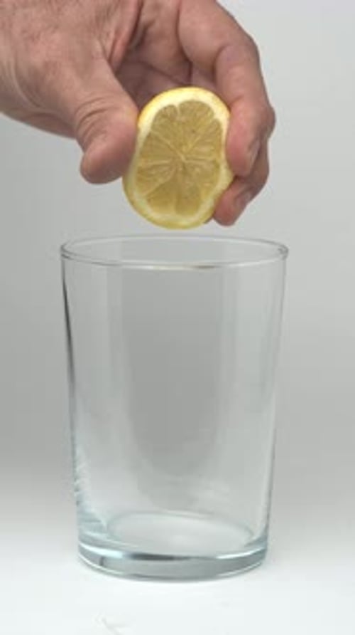 Squeezing Lemon into Glass for Refreshing Drink