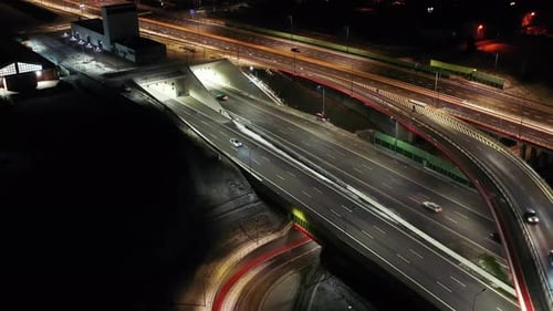 Vue prise par drone de la circulation nocturne sur une autoroute montrant des voitures et des voies de lumière avec un tunnel et des viaducs o