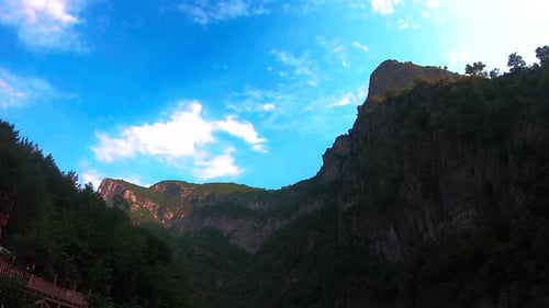 Peaceful top mountains with big cliffs and green trees forest under bright blue sky with white cloud