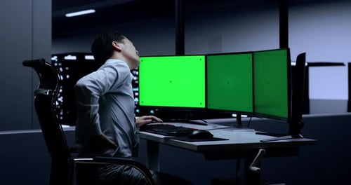 Asian Male Programmer Having A Backache While Typing On Green Screen Desktops In The Server Room