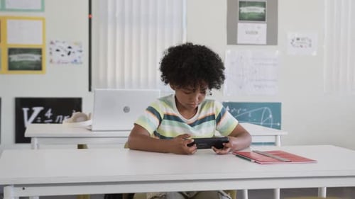 African American teen male tapping handheld device, following cues in class with red folder right