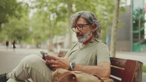 Man Using Phone Sitting on Park Bench