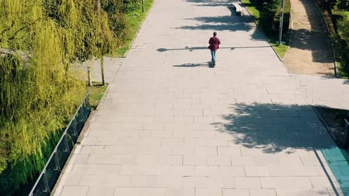 Mann fährt Elektroroller im öffentlichen Park der Stadt an einem sonnigen Sommertag aus der Vogelperspektive Drohne männlich