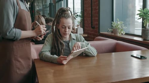 Female Customer Looking Through Menu on Tablet and Making her Order in Cafe