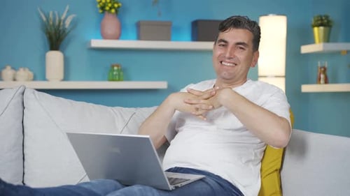 Man Sits on Couch, Uses Laptop, Gestures to Camera