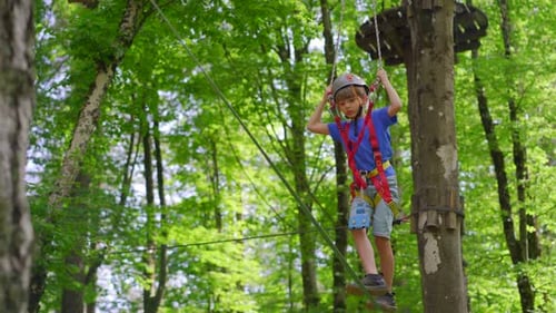 A Little Boy is Enjoying an Exciting Adventure on a Rope Obstacle Course in a Lush Forest