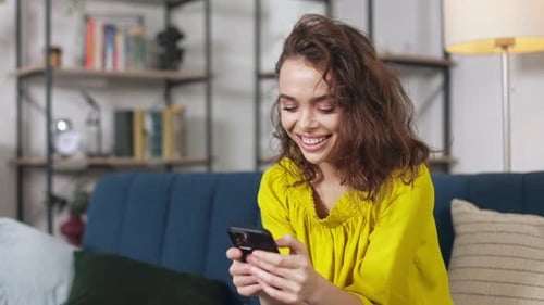 Young Woman Smiling While Using Her Phone at Home