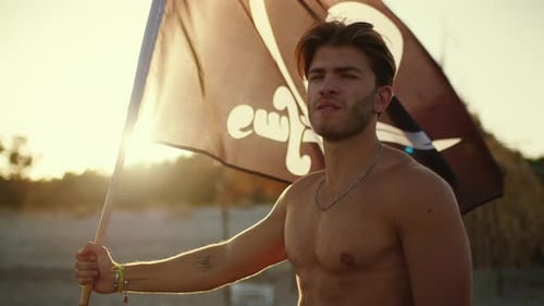 Young Man Holds Pirate Flag on Beach at Sunset