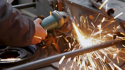 Close-up of a worker grinding metal with sparks flying, in natural light