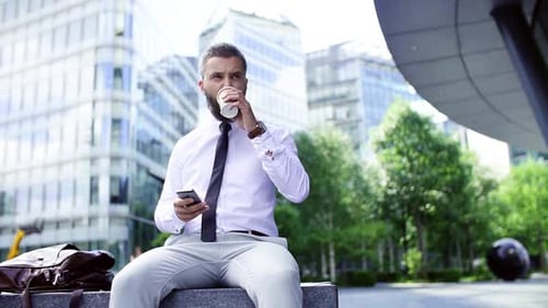 Businessman Sits Using Phone and Having Coffee Break