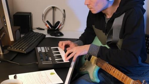 Man Composing on MIDI Keys with Guitar in Studio