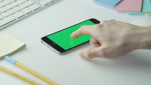 O designer está usando o celular com tela verde no modo paisagem. Vista superior.