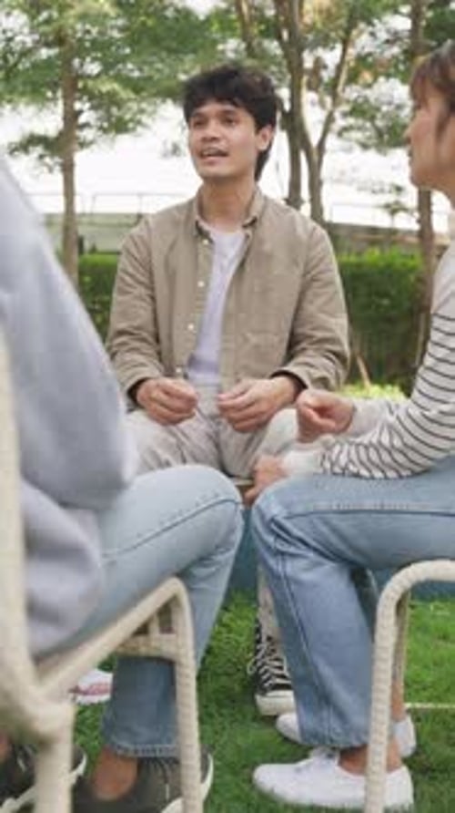 Asian group of people sit in a close circle and talk to therapist in park.