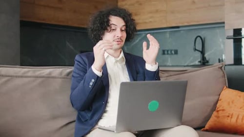 Young Man Explains on Laptop in Apartment