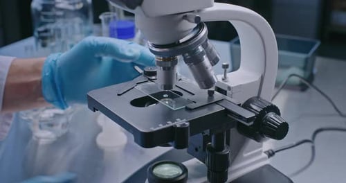 Close Up of Microbiologist Putting Slide with Test Sample Under Microscope