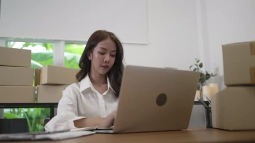 Woman Works on Laptop with Boxes Behind Her