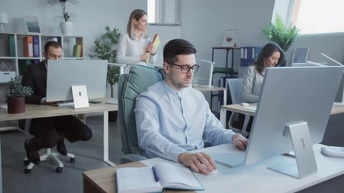 Young Attractive Man Working on Computers i Talking with Colleagues in the Office In the Background