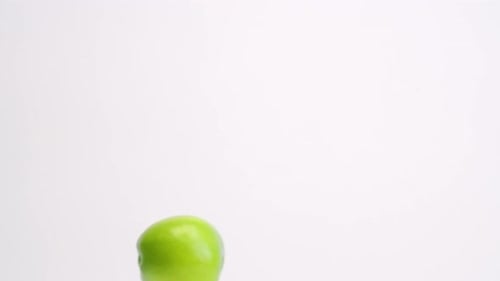 Bright green fresh fruit apples raining down on white backdrop and bouncing back up into frame in sl