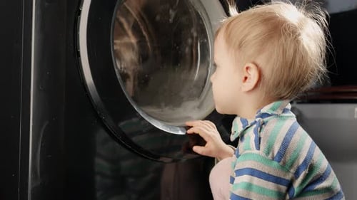 Neugieriges kleines Baby schaut sich zu Hause die Spinntrommel der Waschmaschine an