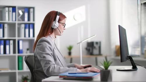 Süße Frau mit Brille arbeitet als Callcenter-Betreiberin und spricht währenddessen mit dem Kunden über ein Headset