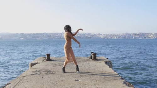 A Young Dancing Woman is Making Performance on a Pier By the Water