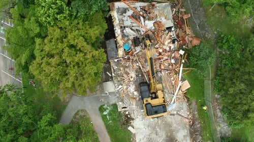 Vue aérienne de haut en bas d'une excavatrice qui démolit une maison dans la banlieue des États-Unis. Des arbres verts en été. Spray pour travailleurs