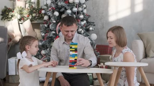 Family Playing Jenga Game by Christmas Tree