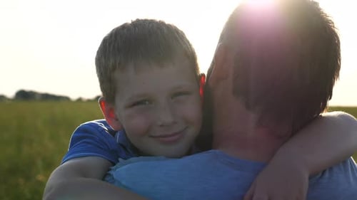 Happy Boy Hugging Father in Sunny Field