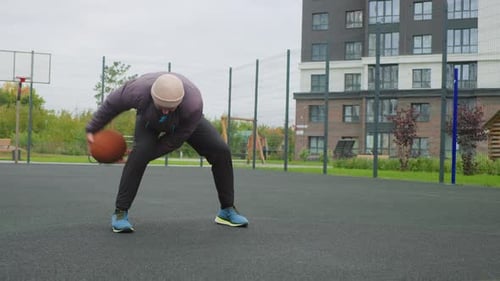 Man Practices Dribbling Basketball on Outdoor Court