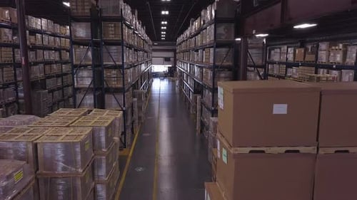 Forward aerial shot of boxes stacked tall in industrial warehouse