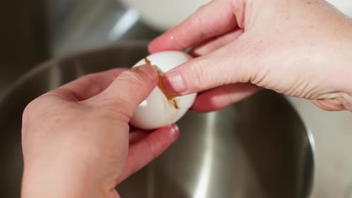 Close Up of Person Cracking Egg Carefully Over Stainless Bowl for Baking