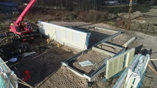 Toma aérea de una grúa posicionando el panel de una casa en una obra